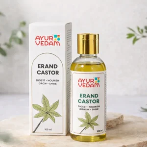 A bottle of Cold Pressed Erand Castor Oil by Ayurvedam 100ml placed on a wooden table,with few castor leaves in the background