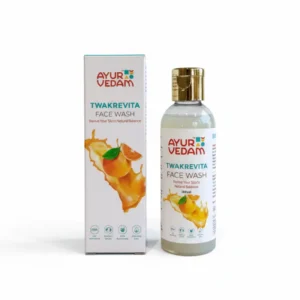 A 100ml bottle and matching box of Ayurvedam Twakrevita Face Wash. The packaging is white with a gold flip-top cap and features an illustration of a fresh orange splash. The label states "Revive Your Skin's Natural Balance" and displays icons for FDA approval and sulfate-free formula.