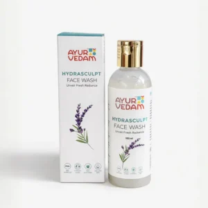 A 100ml bottle and product box for Ayurvedam Hydrasculpt Face Wash, labeled "Unveil Fresh Radiance." The white packaging features a purple lavender sprig illustration and a gold-toned cap. Icons on the bottom indicate it is FDA approved, 100% Ayurvedic, and paraben-free.