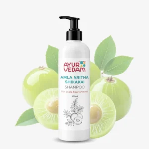 A 100ml white pump bottle of Ayurvedam Amla Aritha Shikakai Shampoo for scalp nourishment, featuring a background of fresh green amla (Indian gooseberry) fruits and leaves.