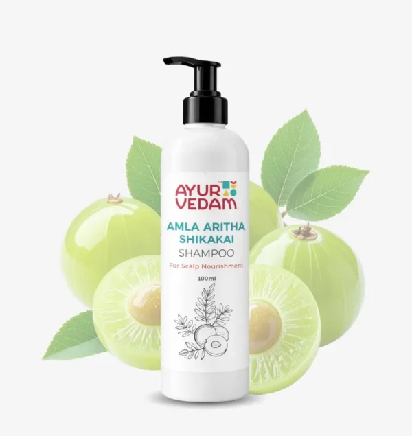 A 100ml white pump bottle of Ayurvedam Amla Aritha Shikakai Shampoo for scalp nourishment, featuring a background of fresh green amla (Indian gooseberry) fruits and leaves.