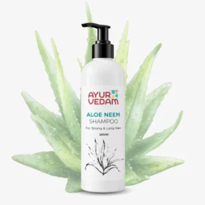 A 100ml white pump bottle of Ayurvedam Aloe Neem Shampoo for strong and long hair, pictured in front of fresh, water-droplet-covered aloe vera leaves.