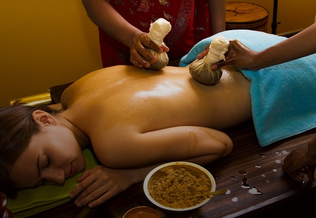 A woman receiving a specialized Ayurvedic back treatment with potli massage and herbal mixture, promoting relaxation and rejuvenation.