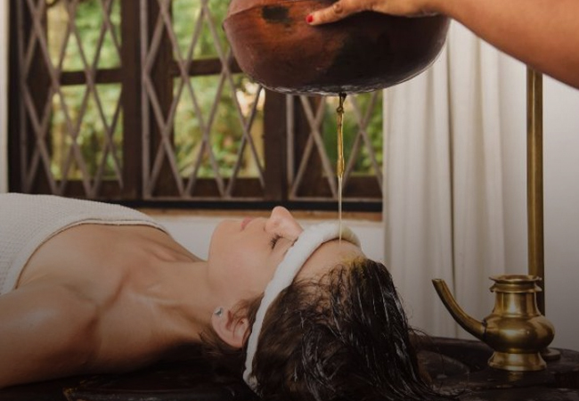 Person receiving Ayurvedic Shirodhara Khada treatment with warm oil pouring on forehead for relaxation and mental clarity.