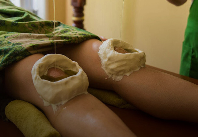 Person at Ayurvedam Store receiving an Ayurvedic Janu Basti treatment with herbal packs on knees.