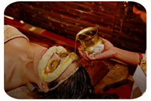 A person is lying down and enjoying a calming Ayurvedic treatment at Ayurvedam Store. Oil is being poured gently from a small brass cup onto their eyes and forehead.